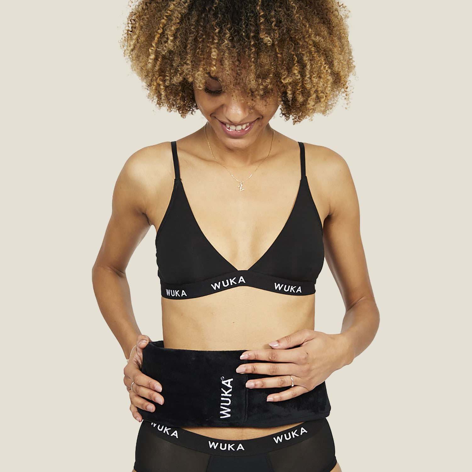 Woman wearing WUKA branded underwear holding a wearable hot water bottle around her waist for period pain relief.