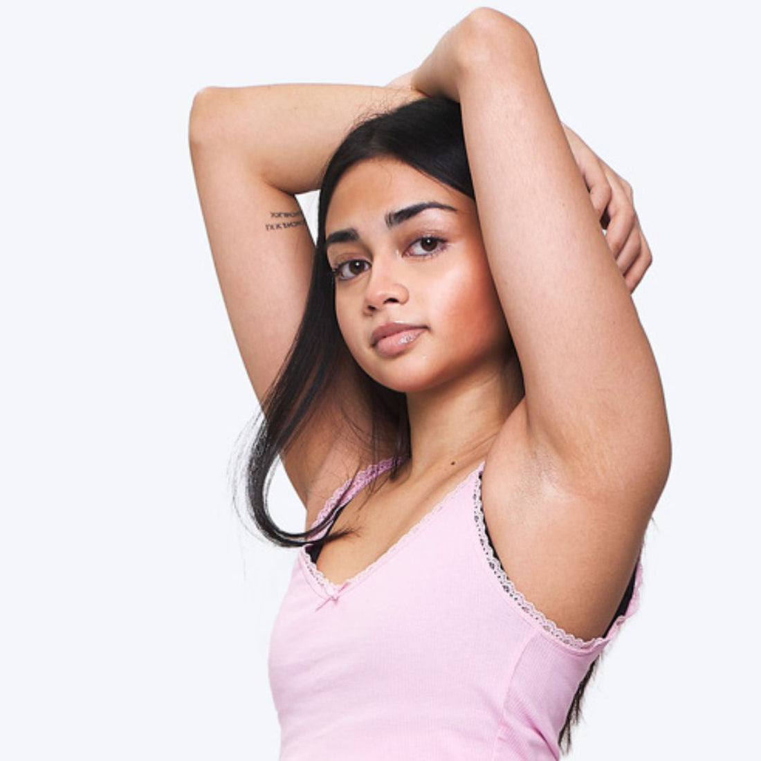 Teen girl in a pink vest with arms raised, looking strong and self-assured—embracing her body, her skin, and her cycle with quiet confidence.