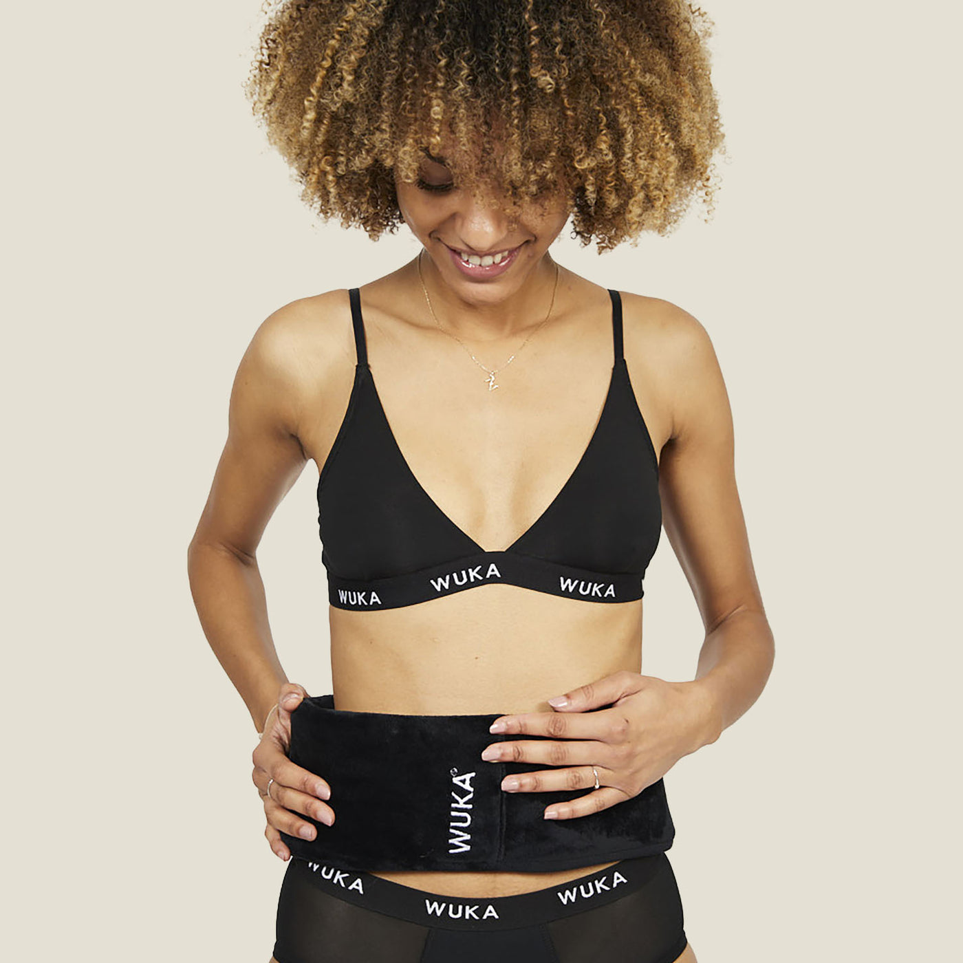 Woman wearing WUKA branded underwear holding a wearable hot water bottle around her waist for period pain relief.