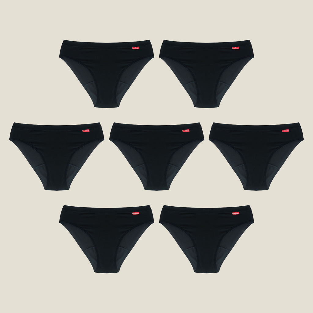 Flat lay of the WUKA Ultimate™ Bikini Medium Flow 7-Pack Period Pants, displayed in a pyramid layout, showing seven black bikini-style period underwear made from soft organic cotton.
