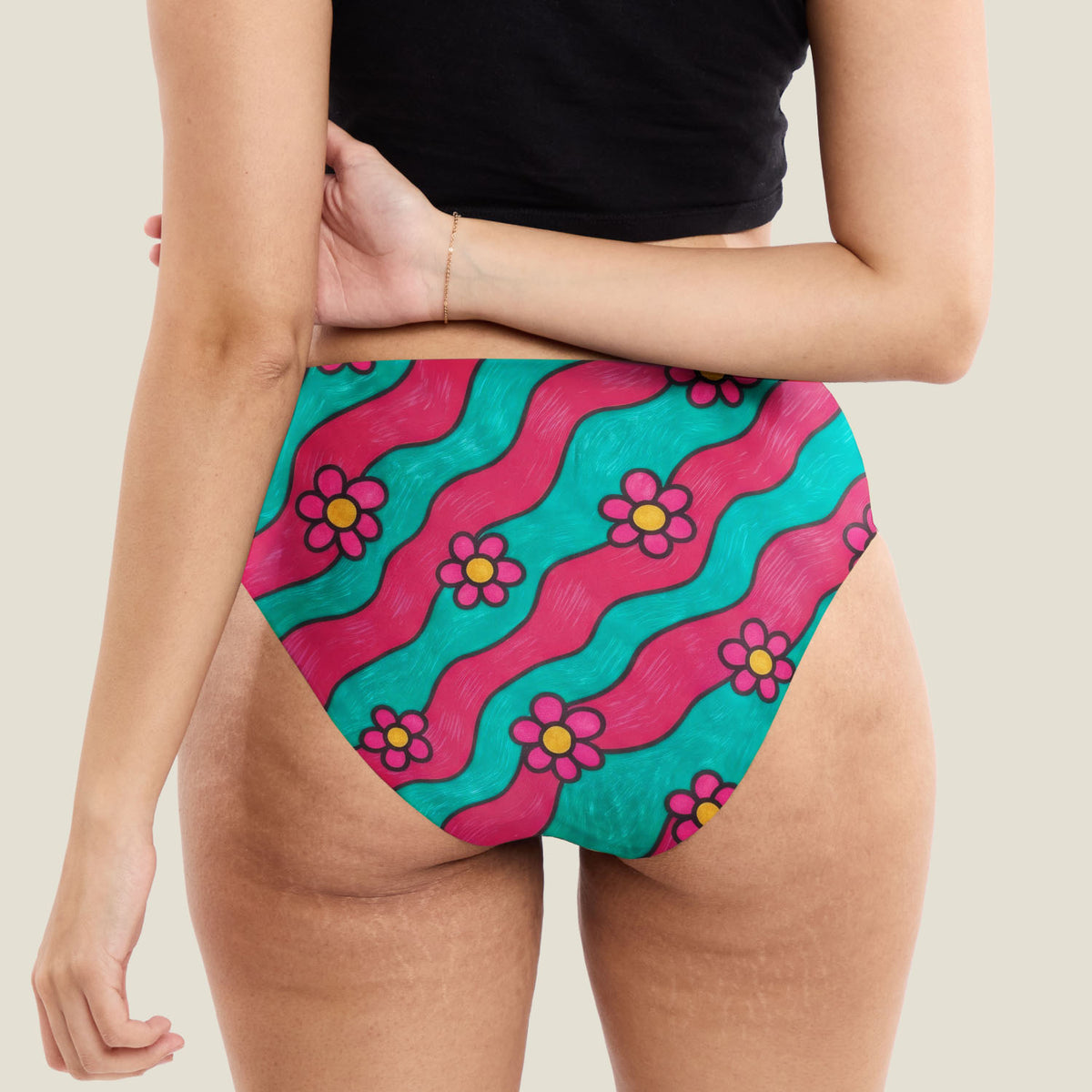 A close-up back shot of a teen model wearing midi brief period pants with a vibrant retro pattern of pink and teal wavy stripes and magenta flowers.