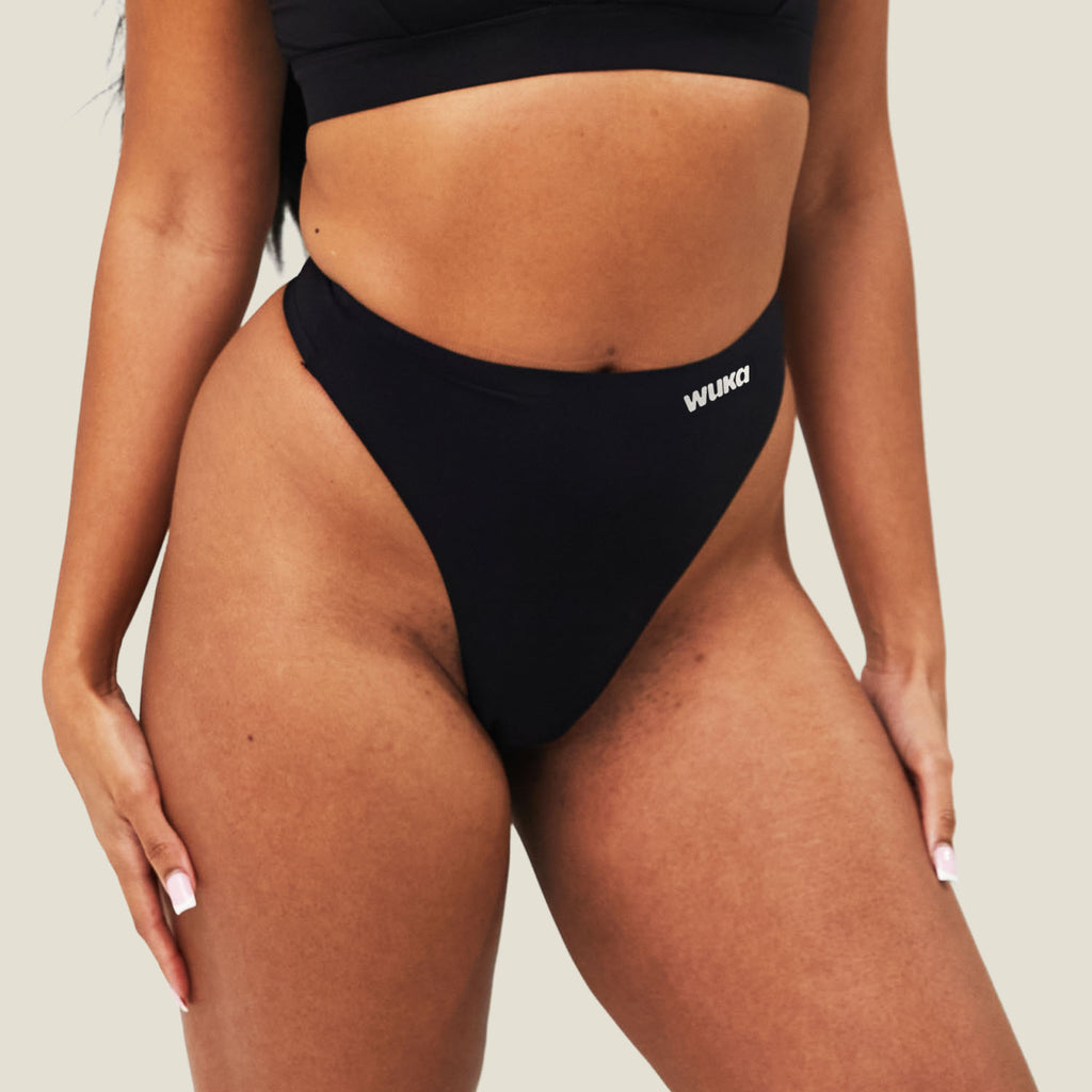 Three-quarter view of the black WUKA Stretch Seamless Mid Period Thong on a model, showing the high-cut leg line and mid-rise waist.