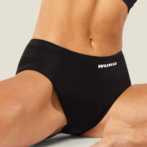 Model seated cross-legged wearing WUKA Stretch™ Midi Brief period underwear for heavy flow, demonstrating stretch and comfort.