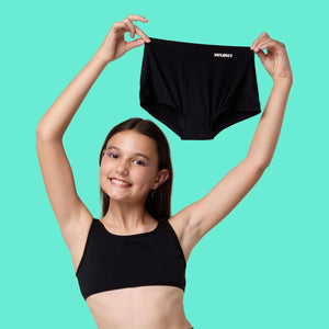 Smiling teen girl holding up WUKA Stretch black period-proof underwear, highlighting back to school offer on leak-proof, size-flexible teen period pants designed for growing bodies and everyday comfort