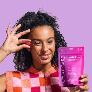 Smiling teen holding a raspberry and WUKA Teen Cycle Care Gummies pouch — vegan-friendly vitamin gummies with Iron and Vitamin C to support energy and reduce fatigue during periods
