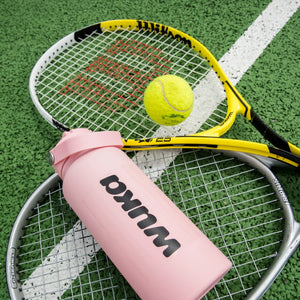 WUKA water bottle and tennis equipment on a sports court, representing period-friendly sports essentials for active girls
