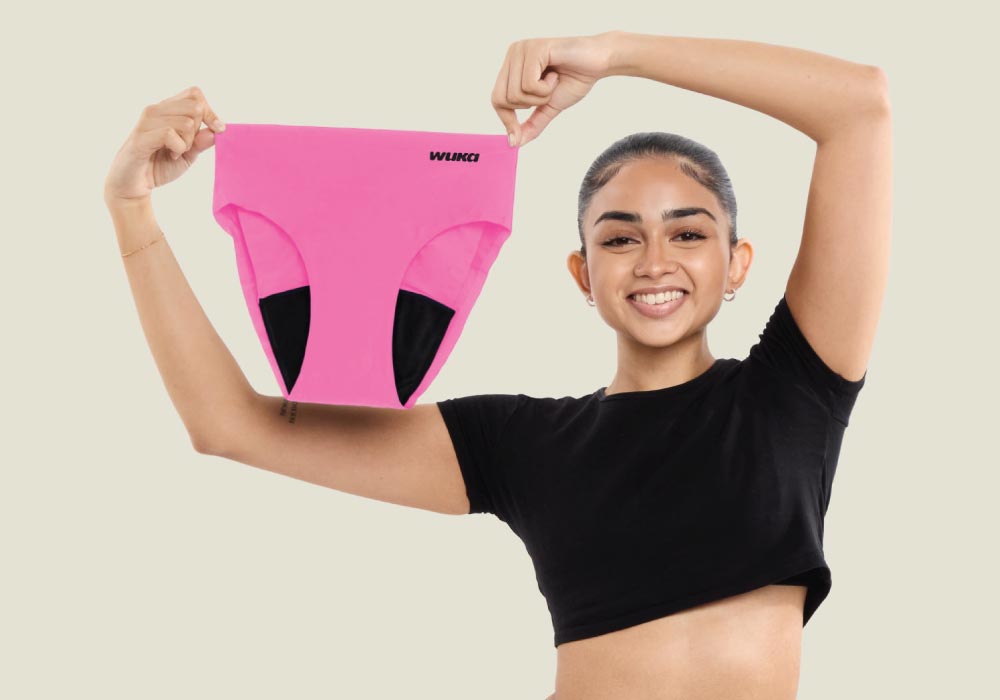 Person holding up pink period pants briefs with a brand logo on a beige background